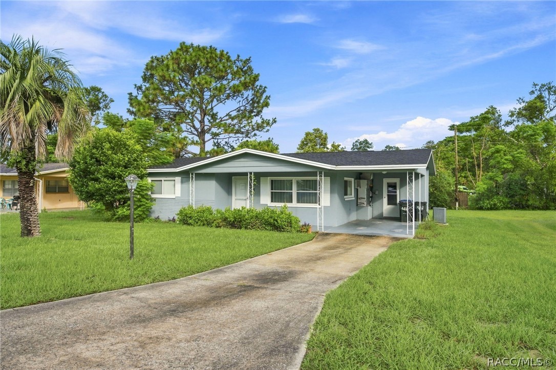 Single-story gray home with a covered entry and concrete driveway across a broad green lawn.