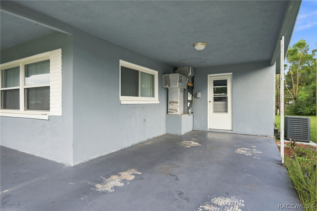Covered concrete patio with gray walls, white-trimmed windows, and exposed utility equipment.