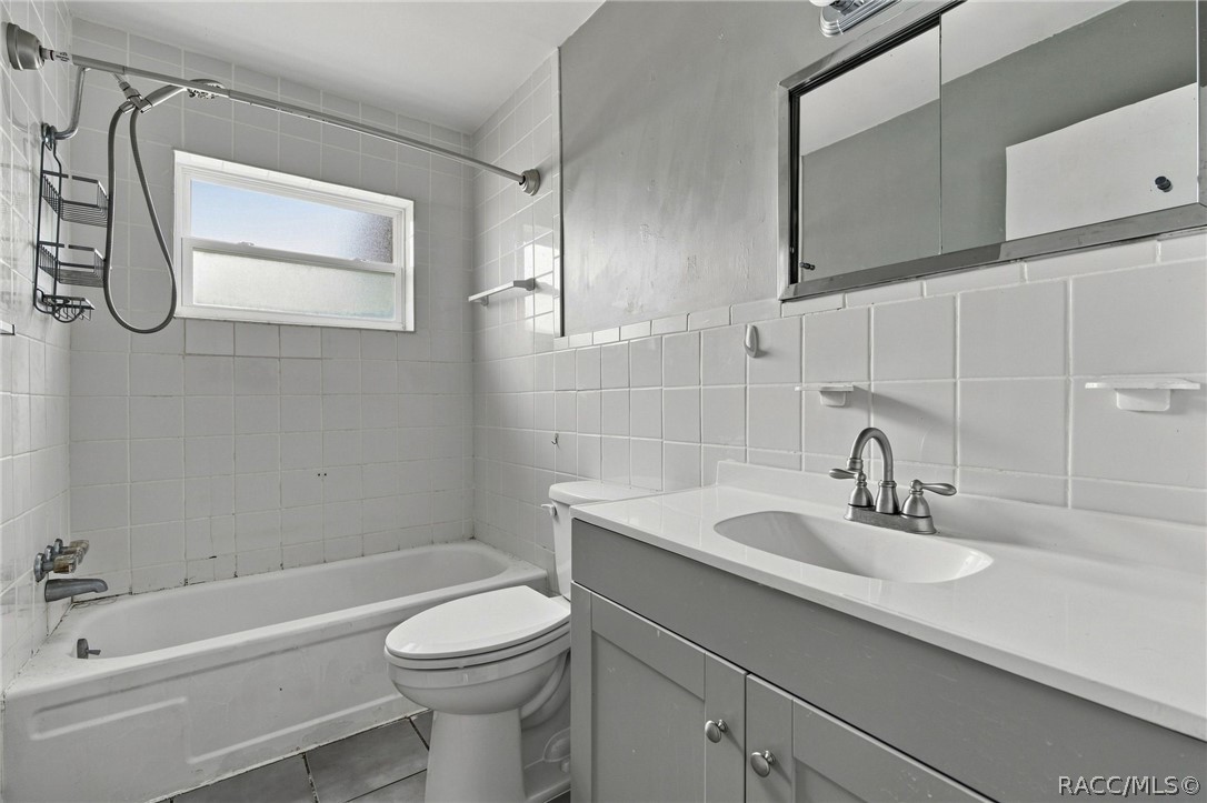 Tiled bathroom with a bathtub and shower, toilet, and white sink vanity beneath a mirrored cabinet.