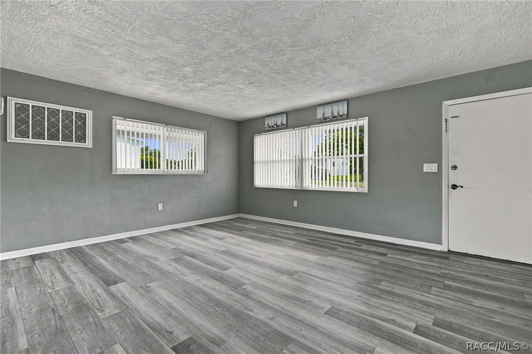 Vacant room with gray plank flooring, two blinded windows, and a wall-mounted air conditioner.