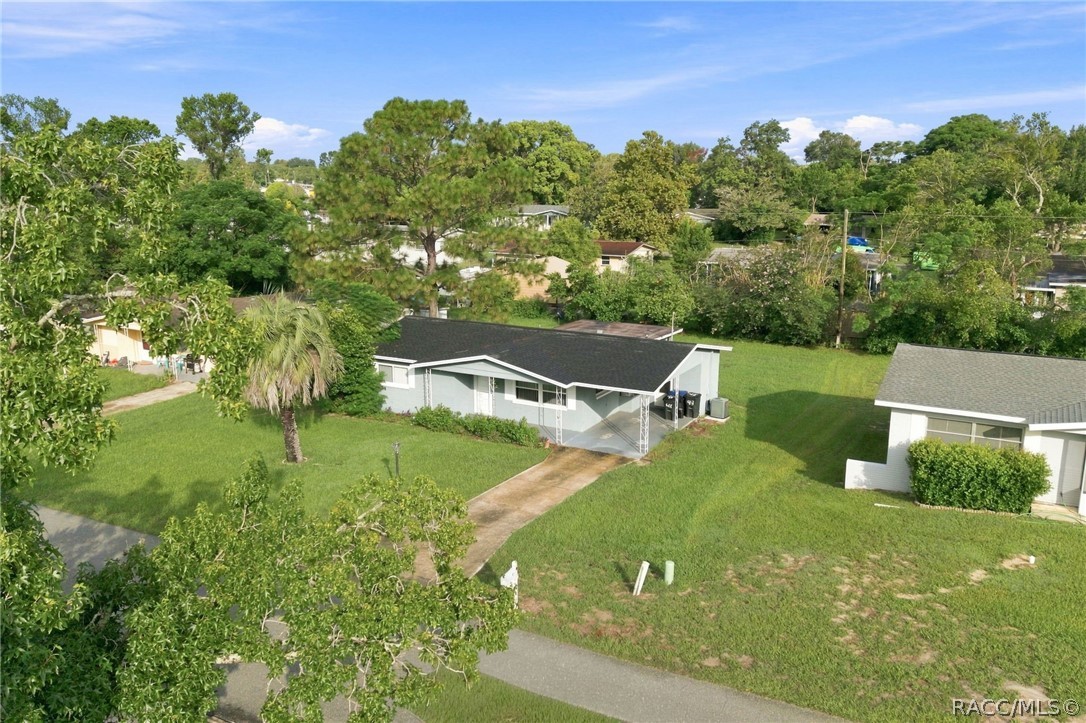 Aerial view of a single-story home with a dark roof, driveway, and broad green lawn.