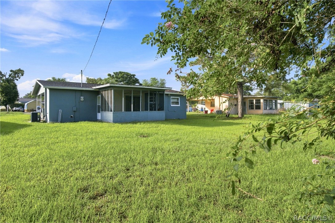 Blue-gray single-story house with a screened porch behind a broad lawn and mature trees.