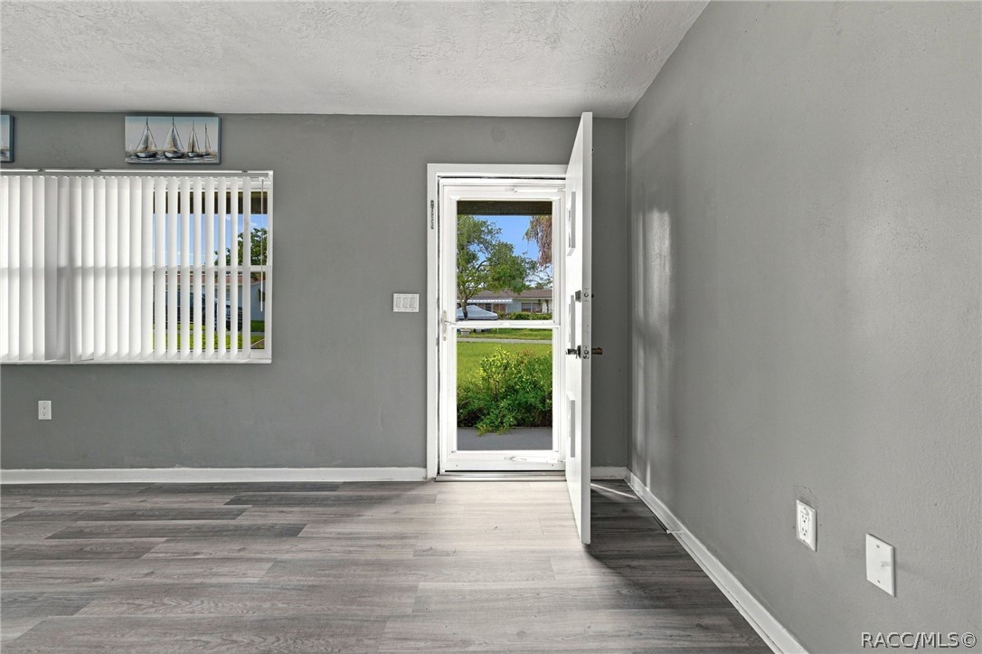Vacant gray room with wood-look flooring, vertical blinds, and an open door to the yard.