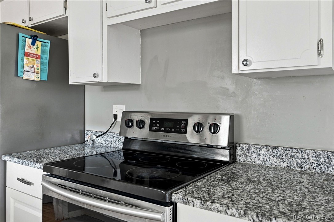 Kitchen with a black glass-top range, speckled granite counters, white cabinets, and gray walls.