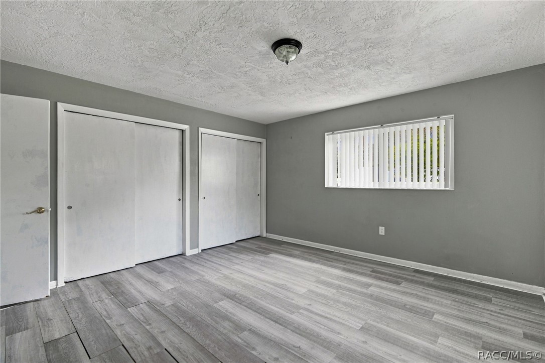 Empty bedroom with gray flooring, two sliding closets, and a window with vertical blinds.