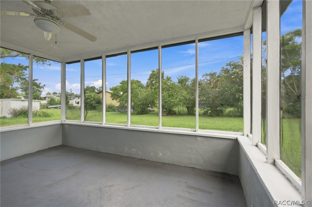 Empty enclosed sunroom with wraparound windows overlooking a green yard.