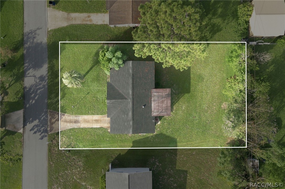 Aerial view of a house and tree-lined grassy lot outlined by a white boundary.