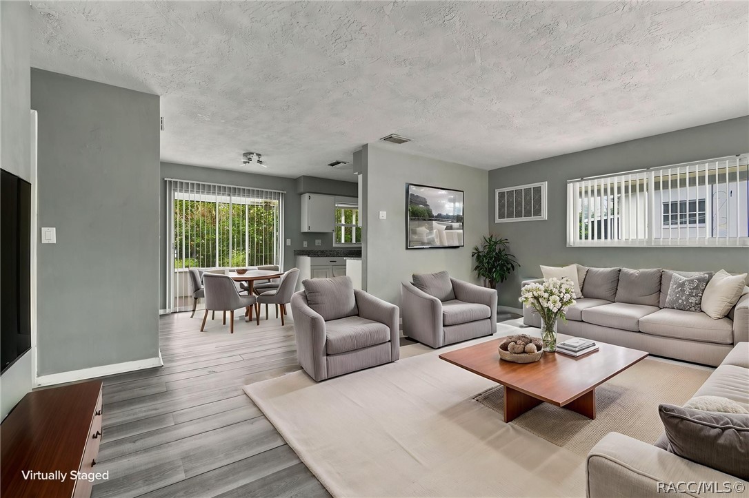 Virtually staged living room with gray seating, a wooden coffee table, and an open dining area.