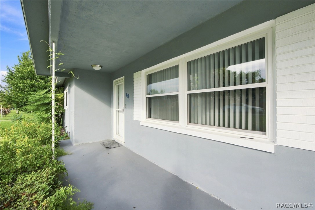 Home exterior with a covered porch, door marked 48, wide windows, and leafy shrubs.