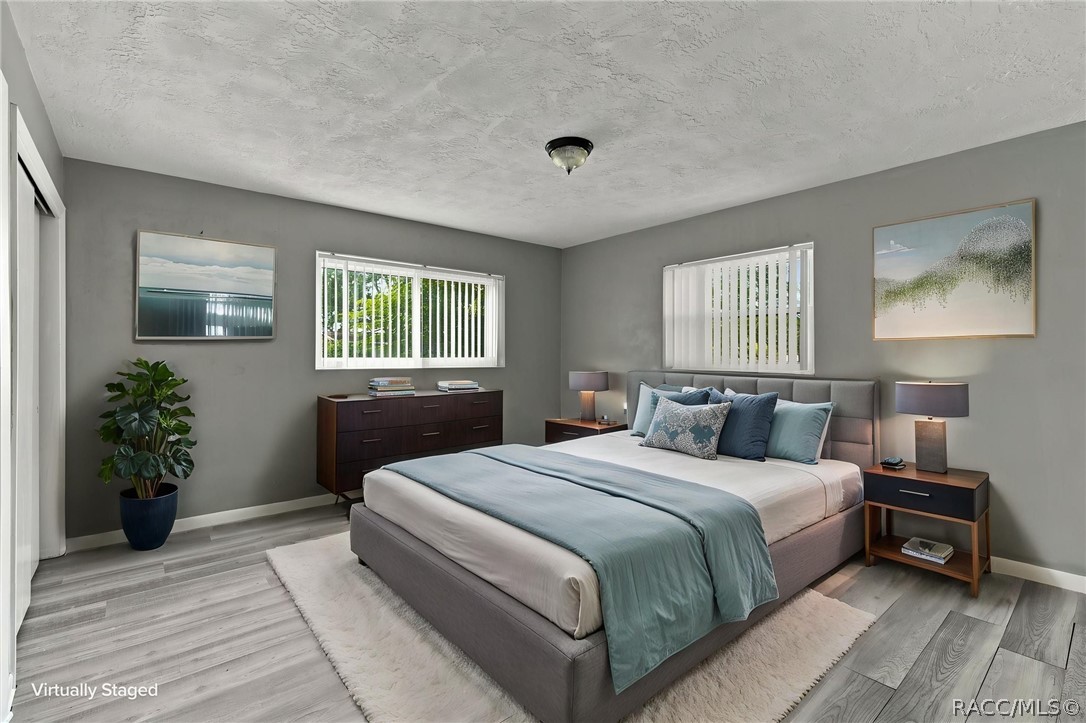 Bedroom with a large gray bed, pale blue bedding, matching nightstands, and a potted plant.