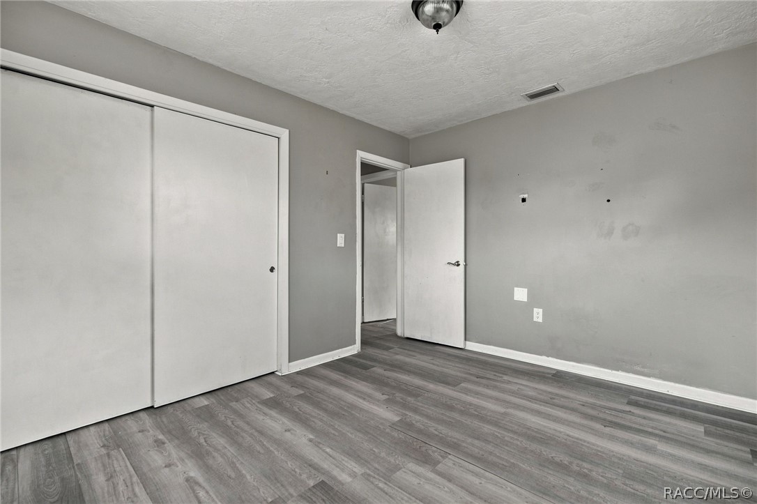 Empty bedroom with gray wood-look floors, a sliding closet, and an open doorway.