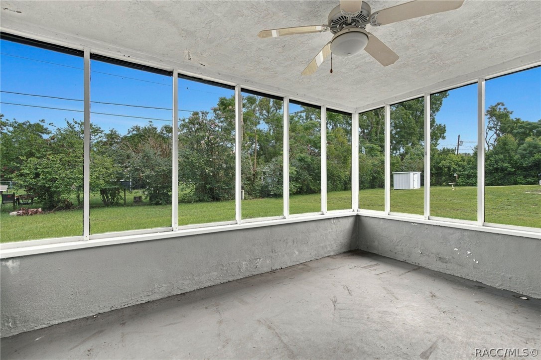 Empty screened porch with a ceiling fan and wide windows overlooking a grassy yard.