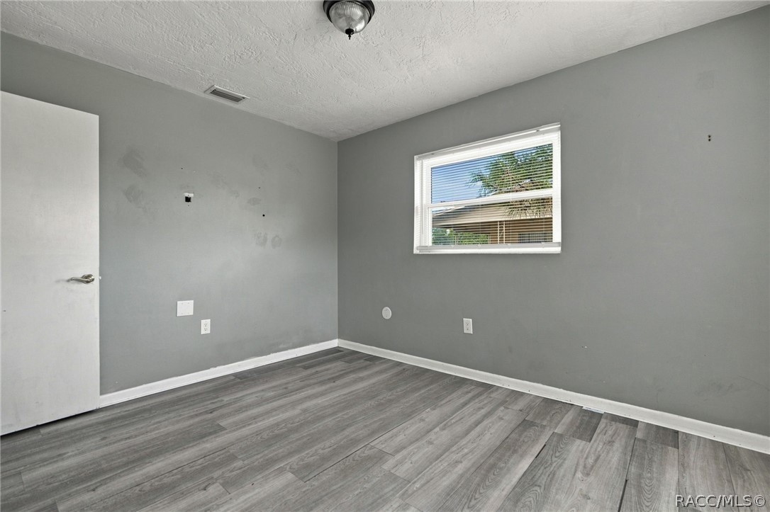 Empty room with gray plank flooring, marked walls, and a small window with blinds.