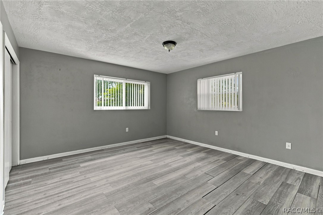 Empty room with gray plank flooring and two windows with vertical blinds.