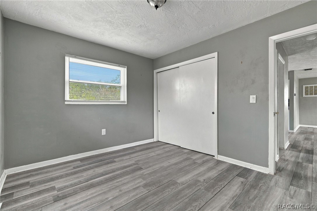 Empty bedroom with gray wood-look flooring, a white sliding-door closet, and a window with blinds.