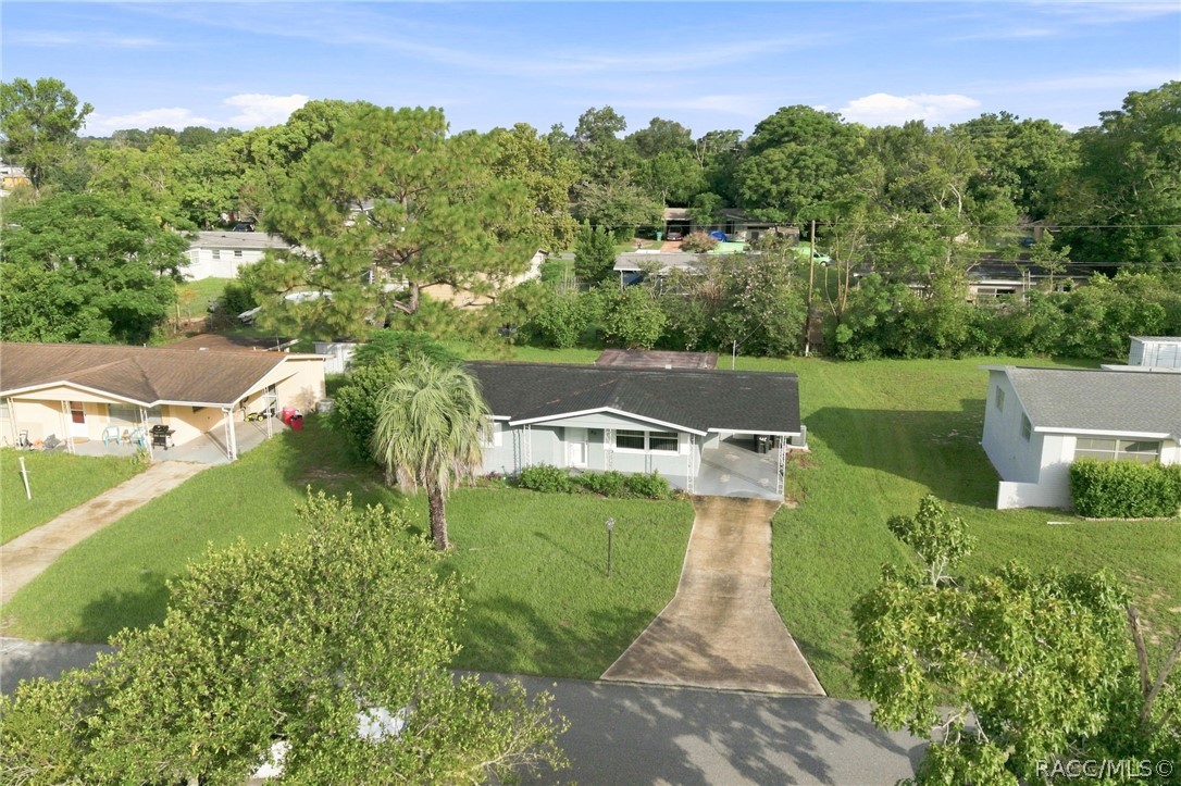Aerial view of a single-story home with a curved driveway, broad lawn, and palm tree.