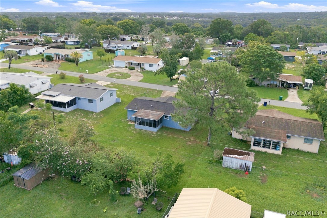 Aerial view of a residential neighborhood with detached homes, green yards, and a wooded horizon.