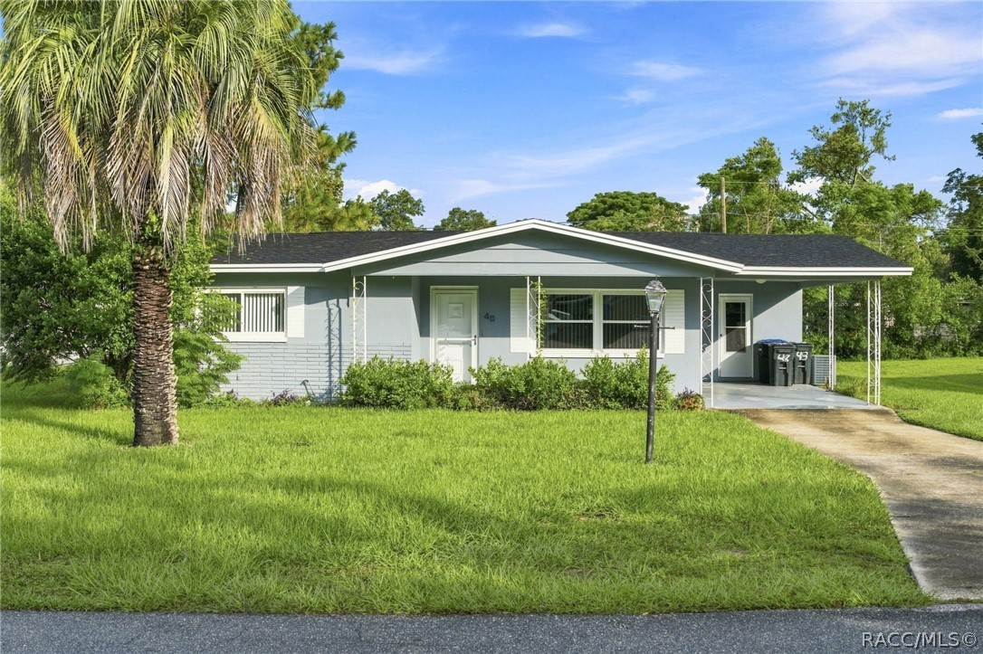 Single-story house with a dark gabled roof, carport, broad lawn, and large palm tree.