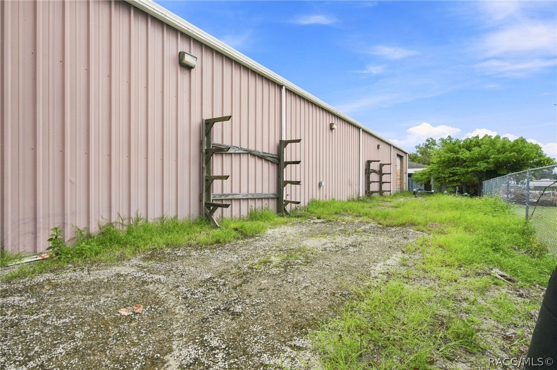 Long metal-sided building beside a gravel-and-grass yard and chain-link fence.