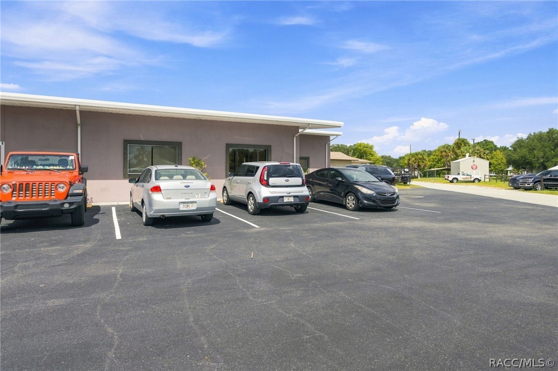Commercial building beside a wide parking lot with several parked cars.