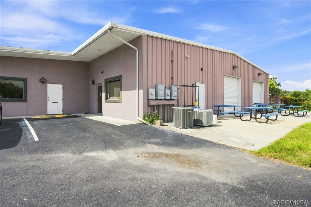 Commercial building with pink metal siding, two roll-up doors, and picnic tables outside.