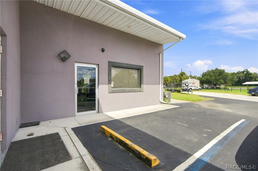 Commercial building exterior with a glass entry, large window, and paved parking area.