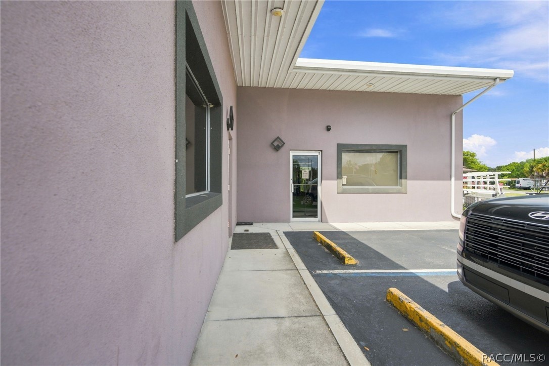 Building entrance with pale pink stucco walls, dark-trimmed windows, and a small parking area.