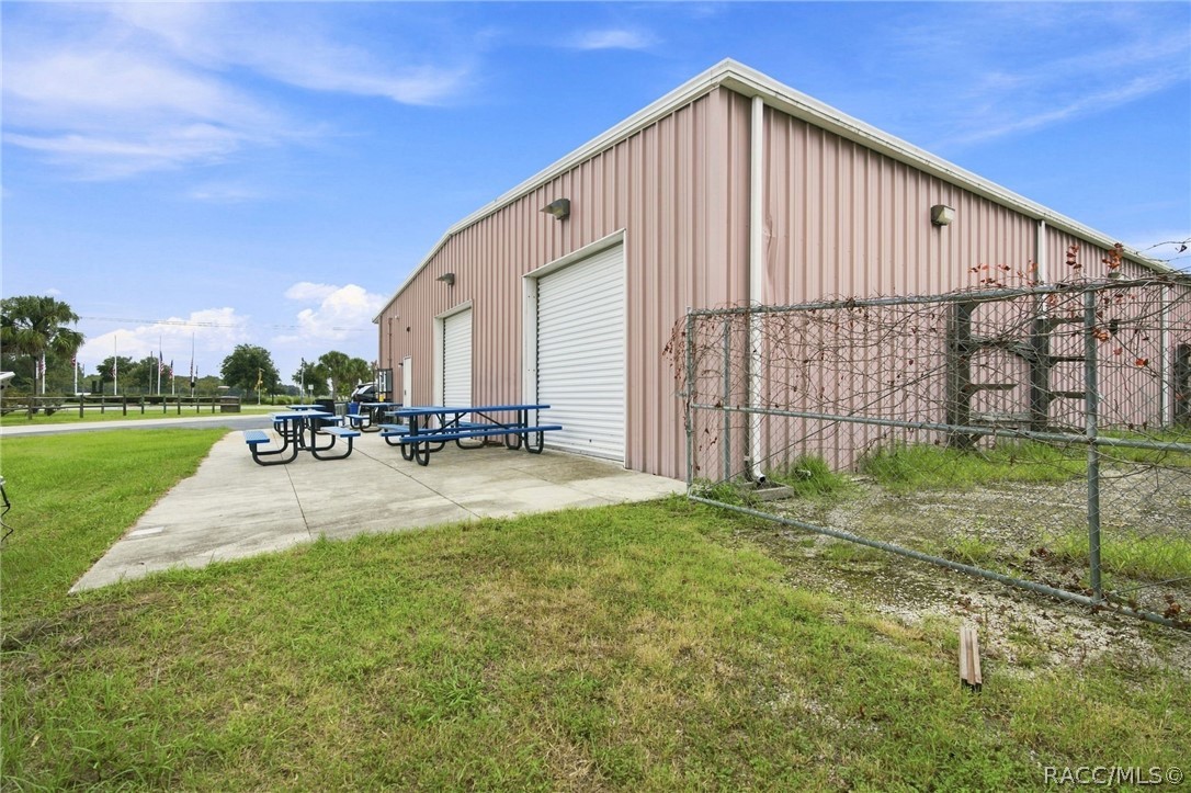 Pink metal-sided commercial building with white roll-up doors, picnic tables, and a chain-link fence.
