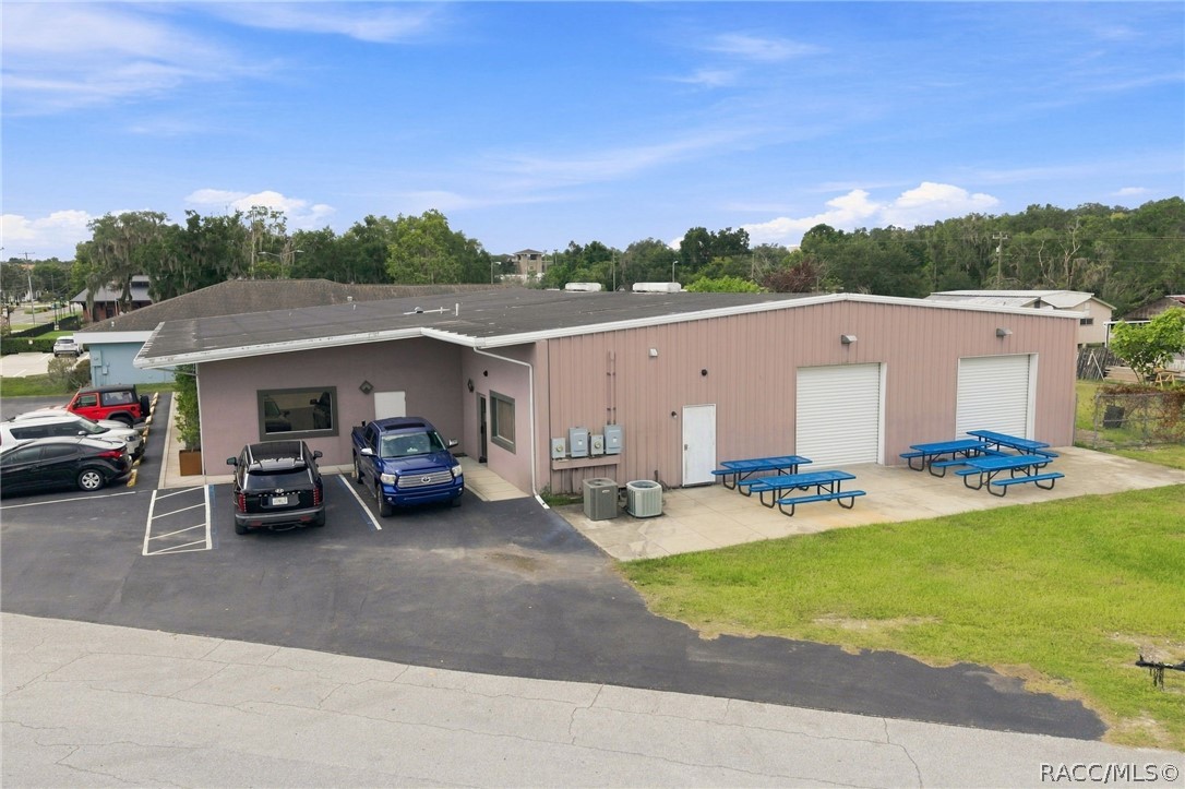 Commercial building with pink siding, two roll-up doors, and blue picnic tables beside the parking area.