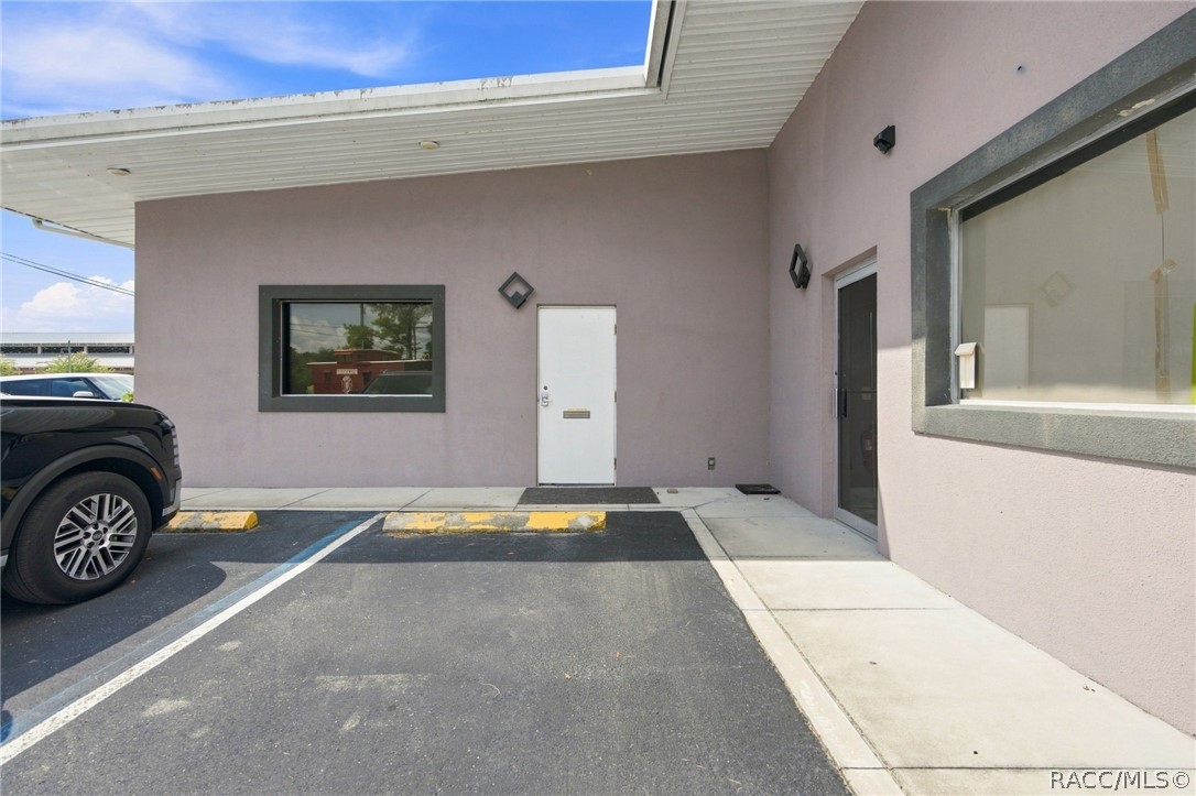 Commercial building entrance with a covered walkway, white door, and parking spaces.
