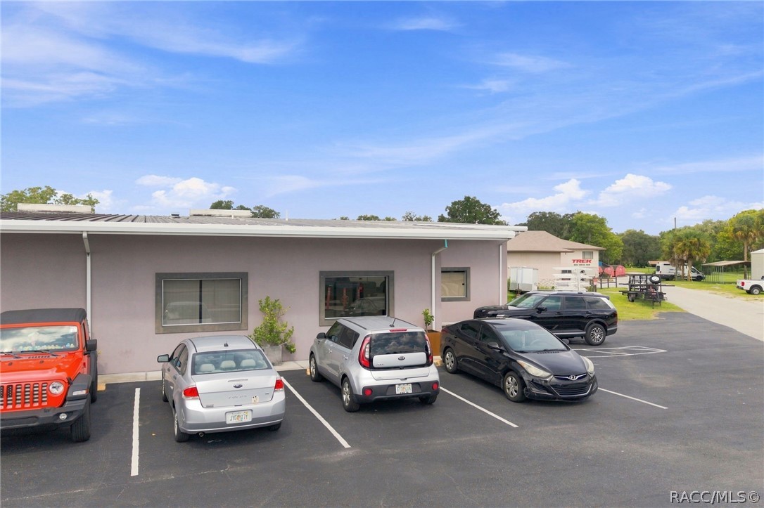 Single-story commercial building with a lavender facade and several cars parked in front.