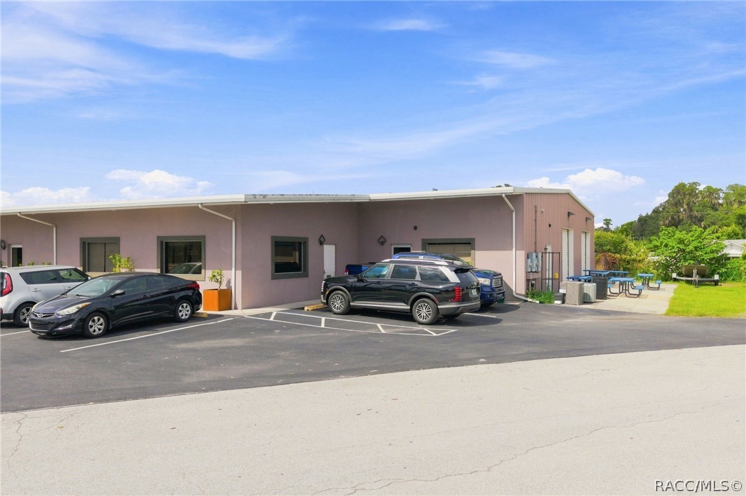 Single-story commercial building with parked cars and picnic tables beside the entrance.