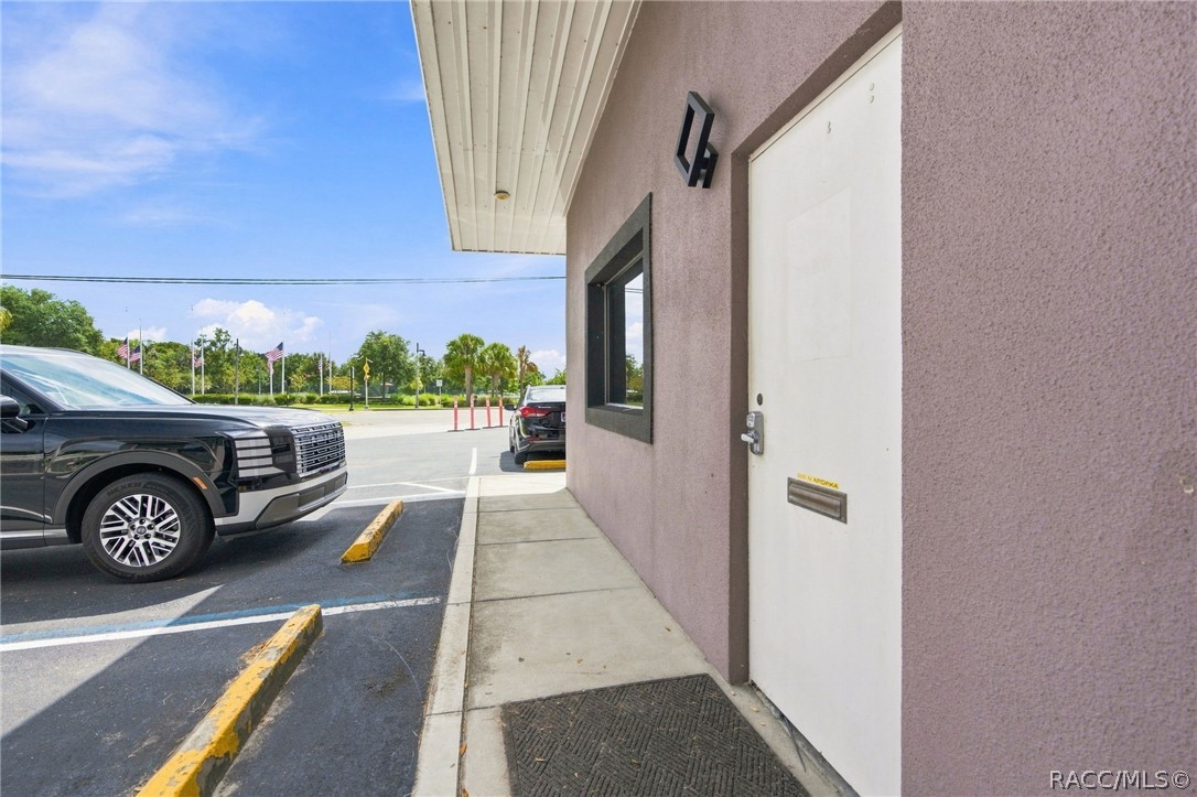 Property entrance with a white door, purple stucco exterior, and adjacent parking area.