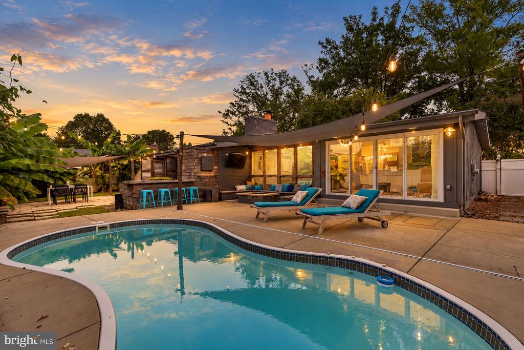 Single-story home with a curved swimming pool and string-lit patio at sunset.