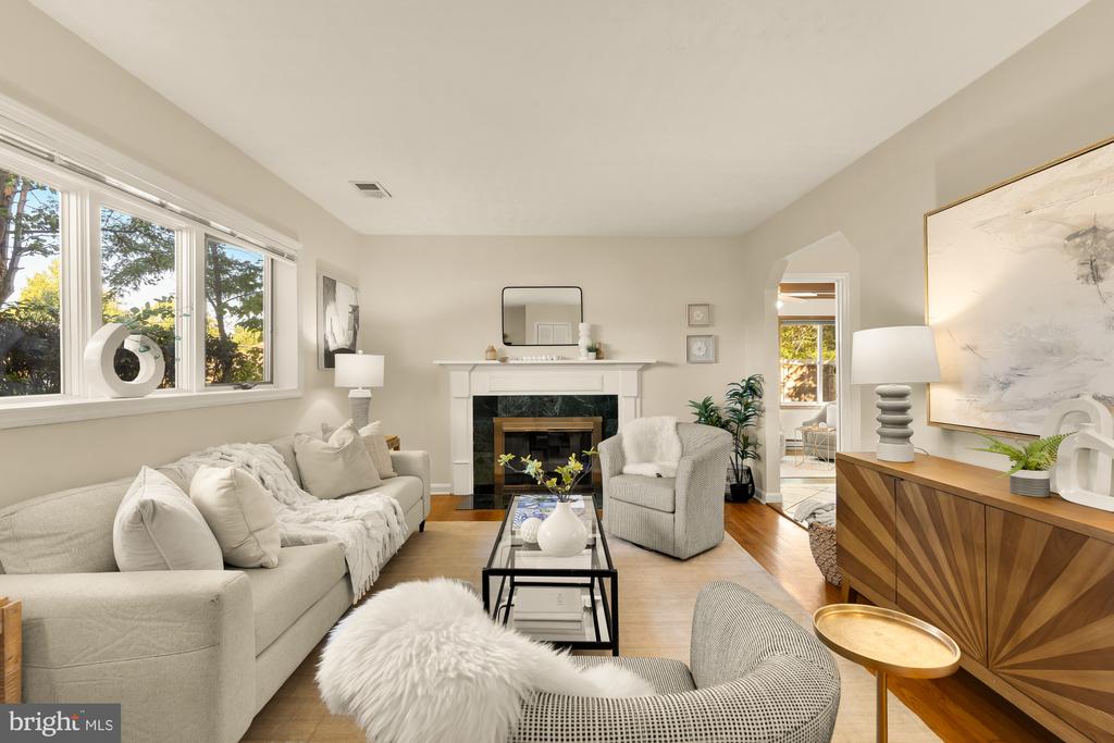 Staged living room with a fireplace, cream seating, large windows, and wood floors.