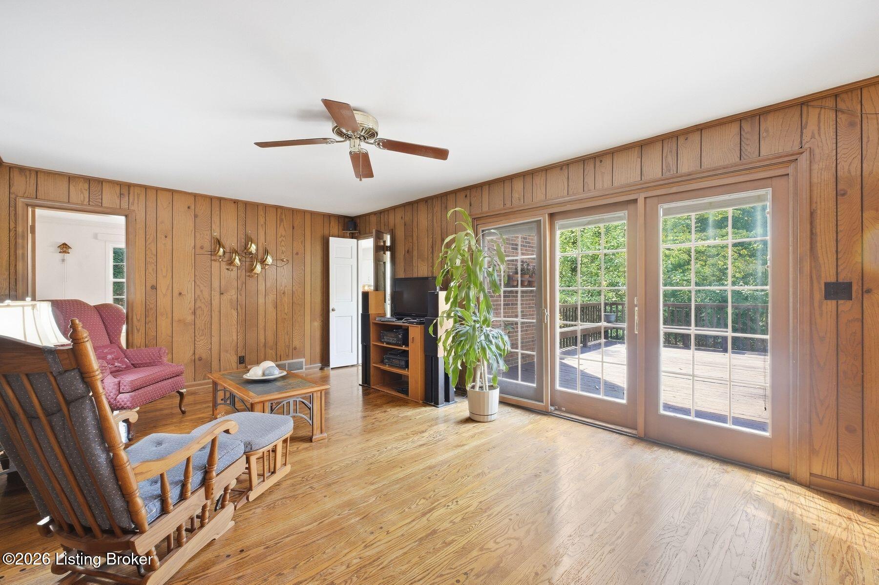 Living room with wood-paneled walls, rocking chairs, and glass doors opening to a deck.