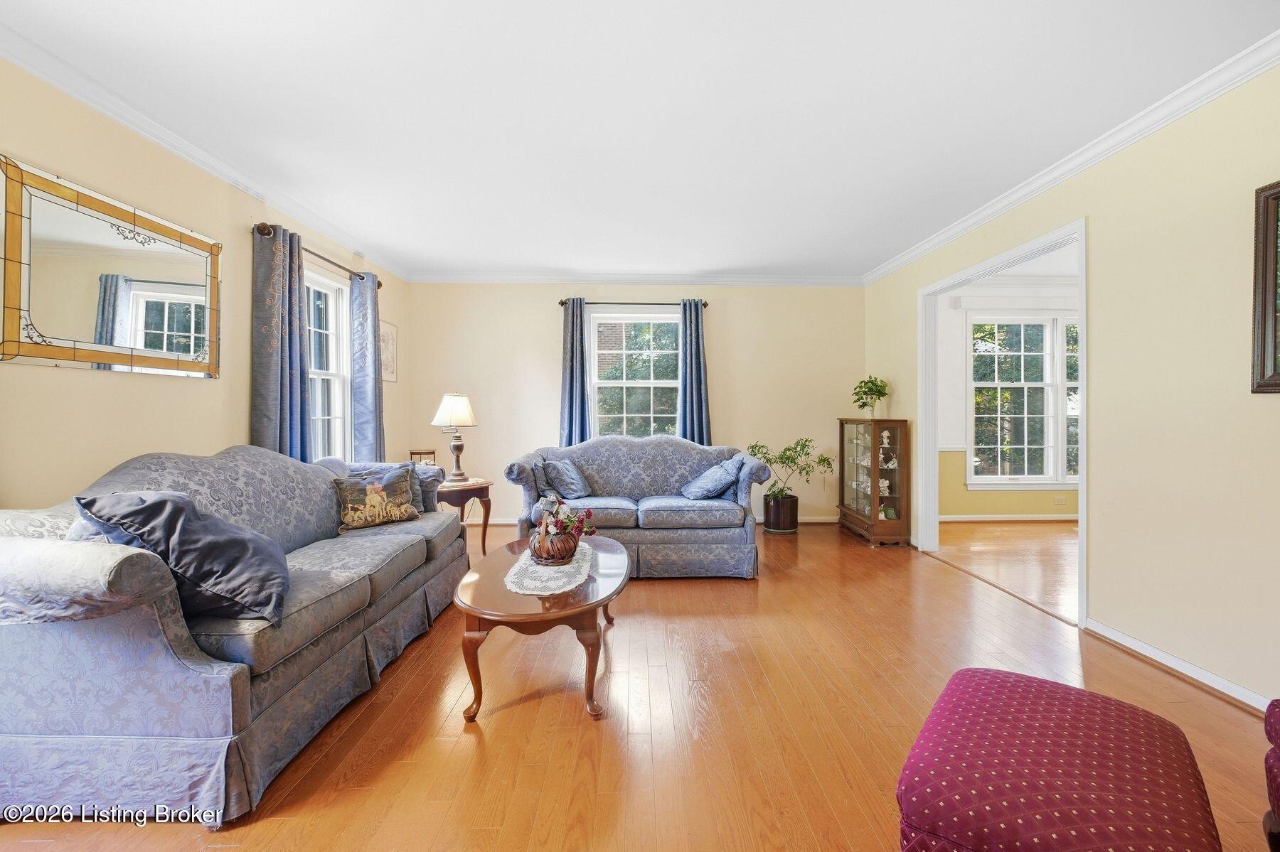 Living room with blue patterned sofas, hardwood floors, and tall curtained windows.
