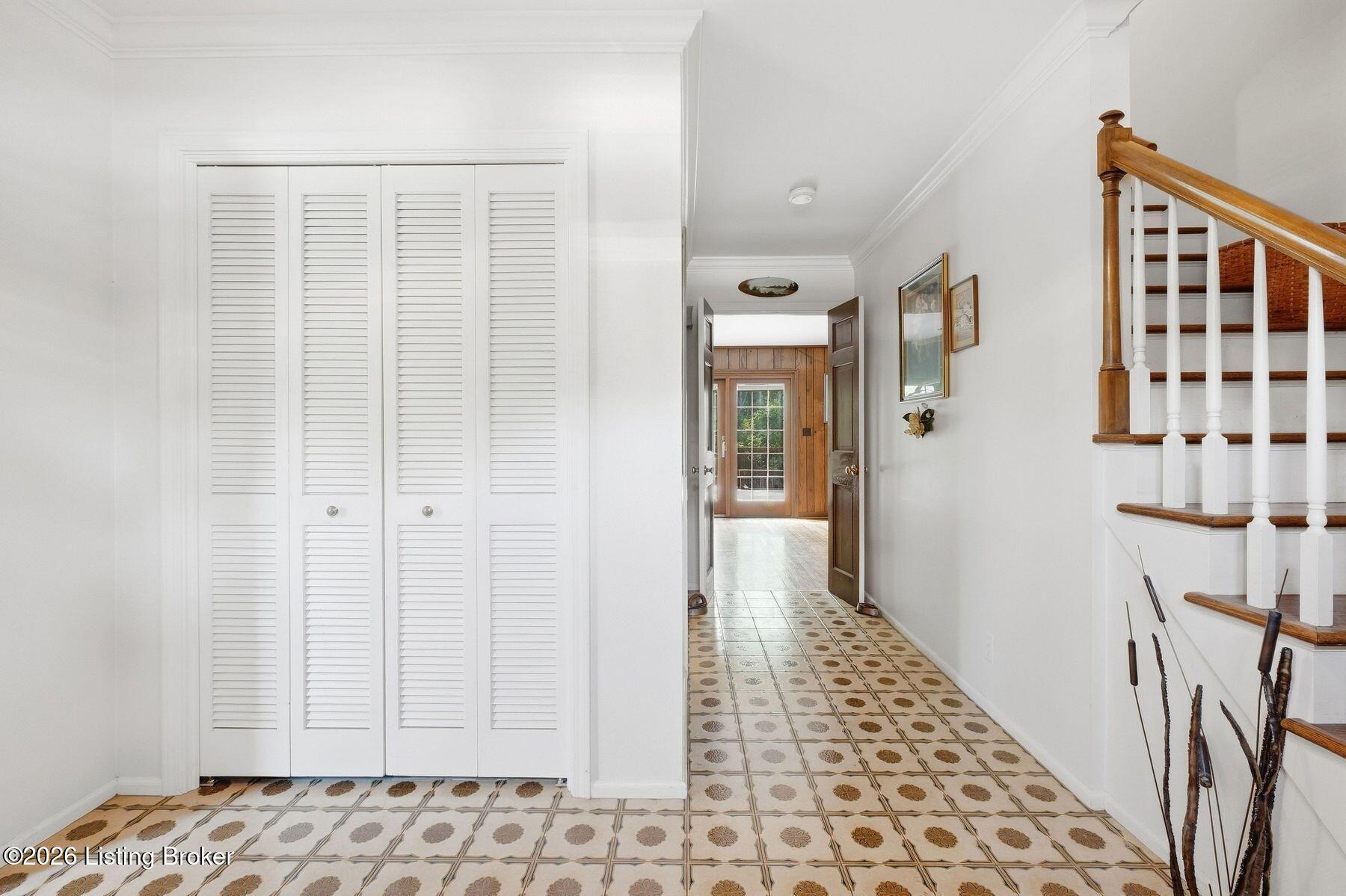 Entry hall with patterned tile floors, louvered closet doors, and a staircase with a wood handrail.