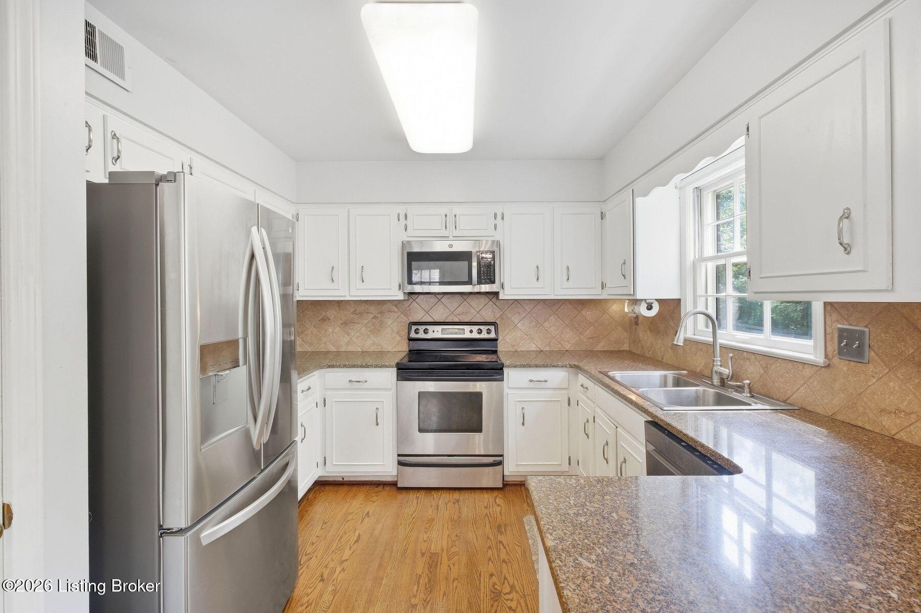 Kitchen with white cabinetry, stainless steel appliances, granite counters, and hardwood flooring.