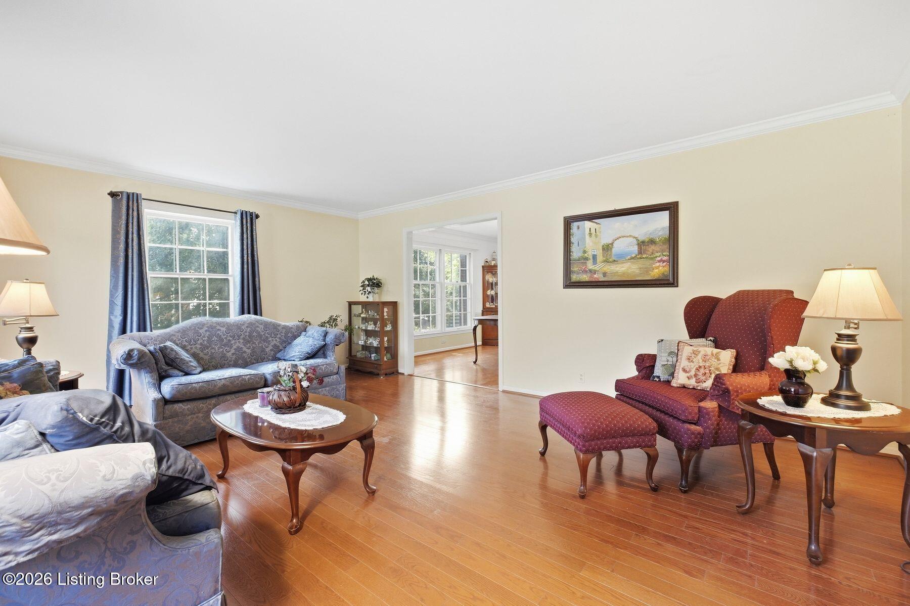 Living room with blue patterned sofas, a burgundy armchair, hardwood floors, and a bright adjoining room.