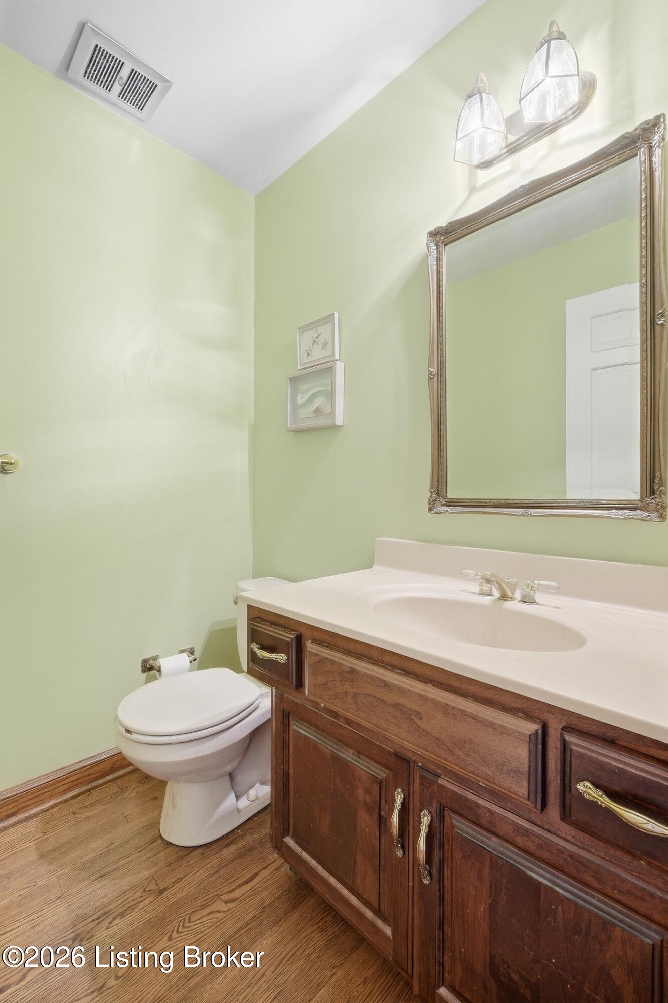 Bathroom with pale green walls, dark wood vanity, framed mirror, and wood flooring.