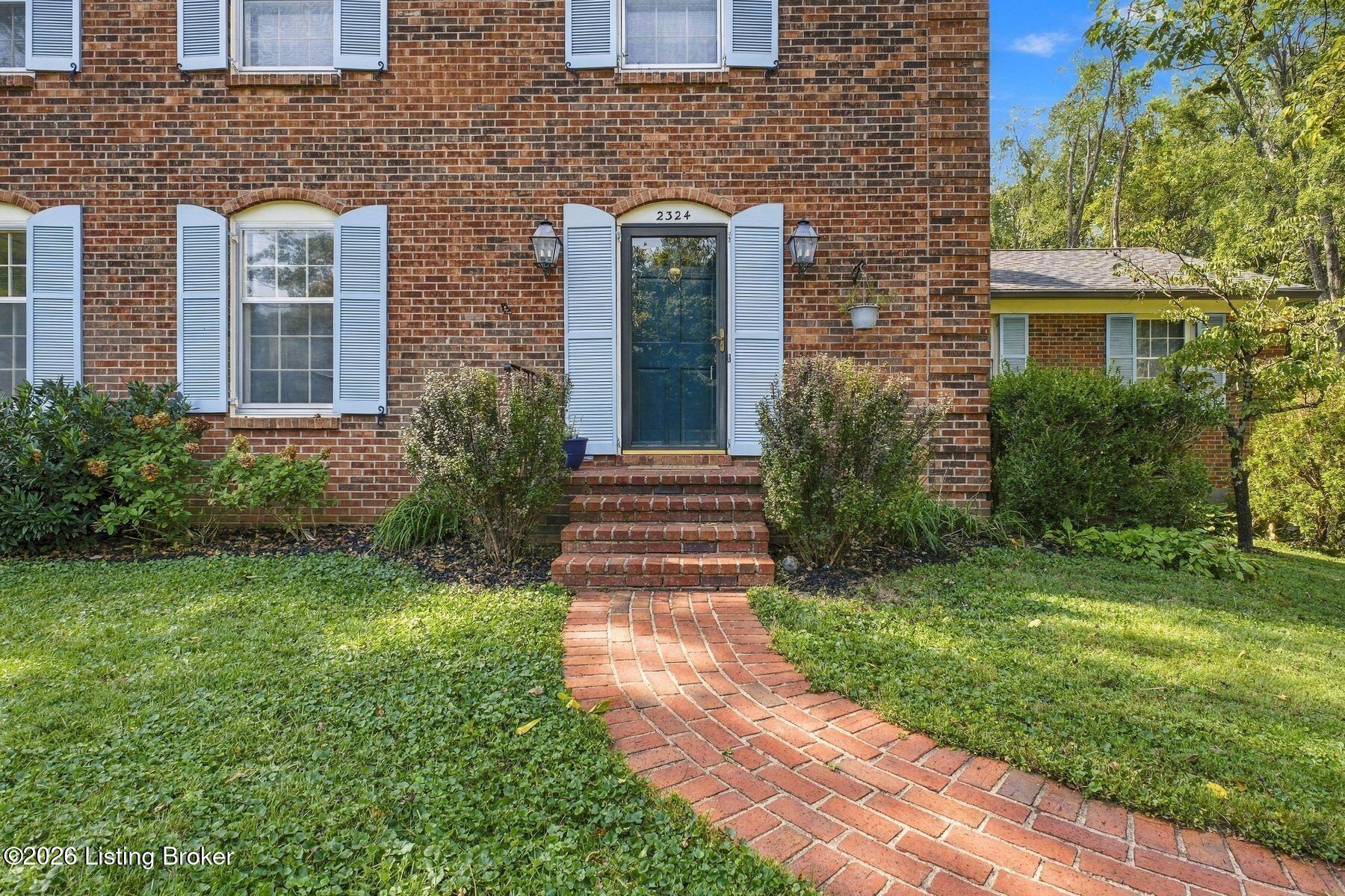 Red brick house with blue shutters and a curved brick walkway leading to the front door.