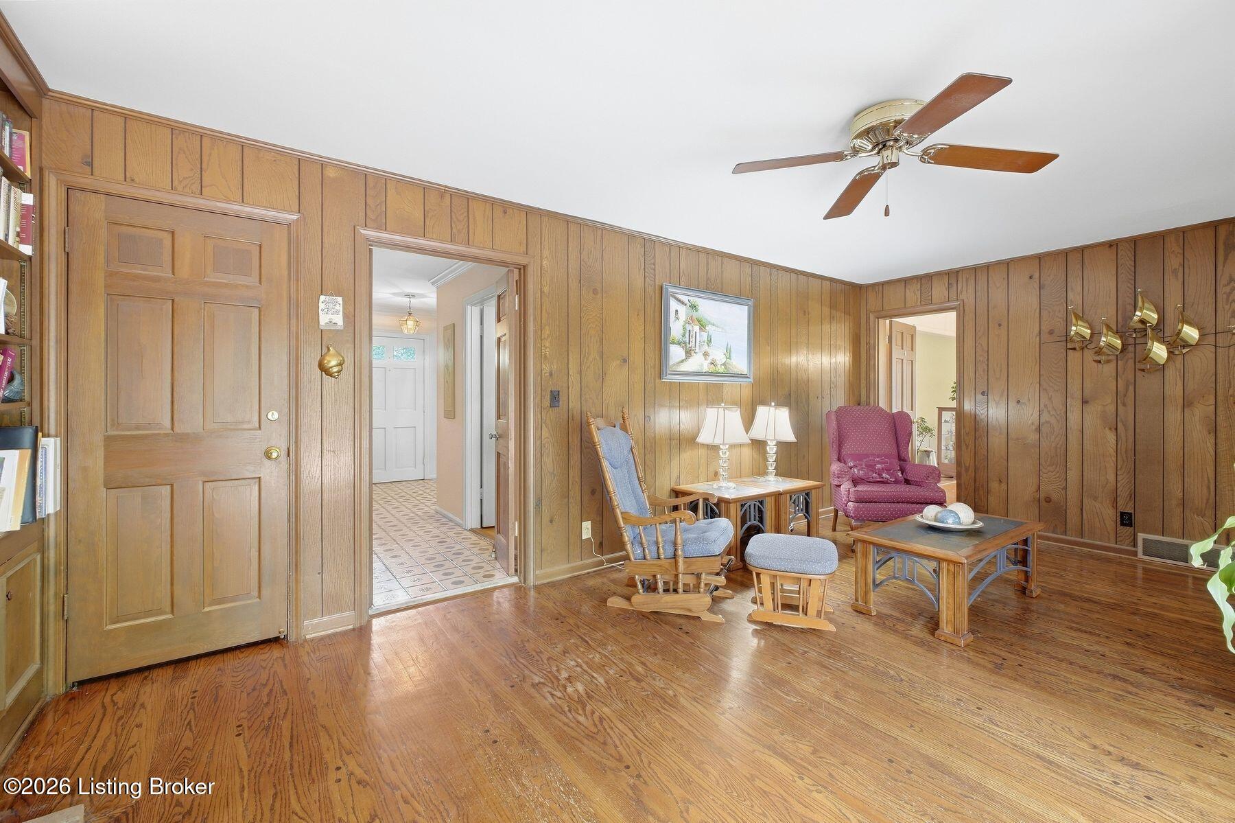 Living room with wood-paneled walls, hardwood floors, rocking chairs, and a pink armchair.