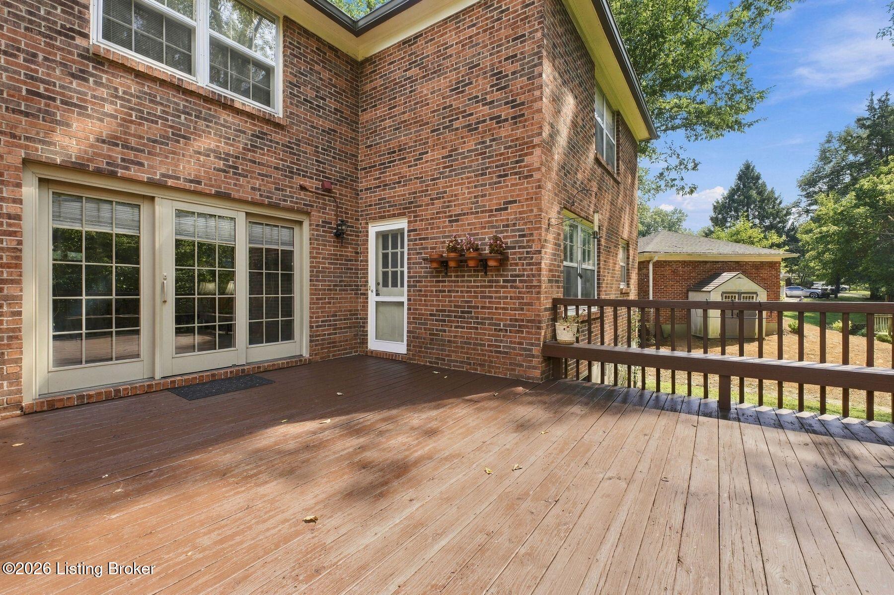 Rear deck of a two-story brick house, with sliding glass doors and a view of a detached outbuilding.