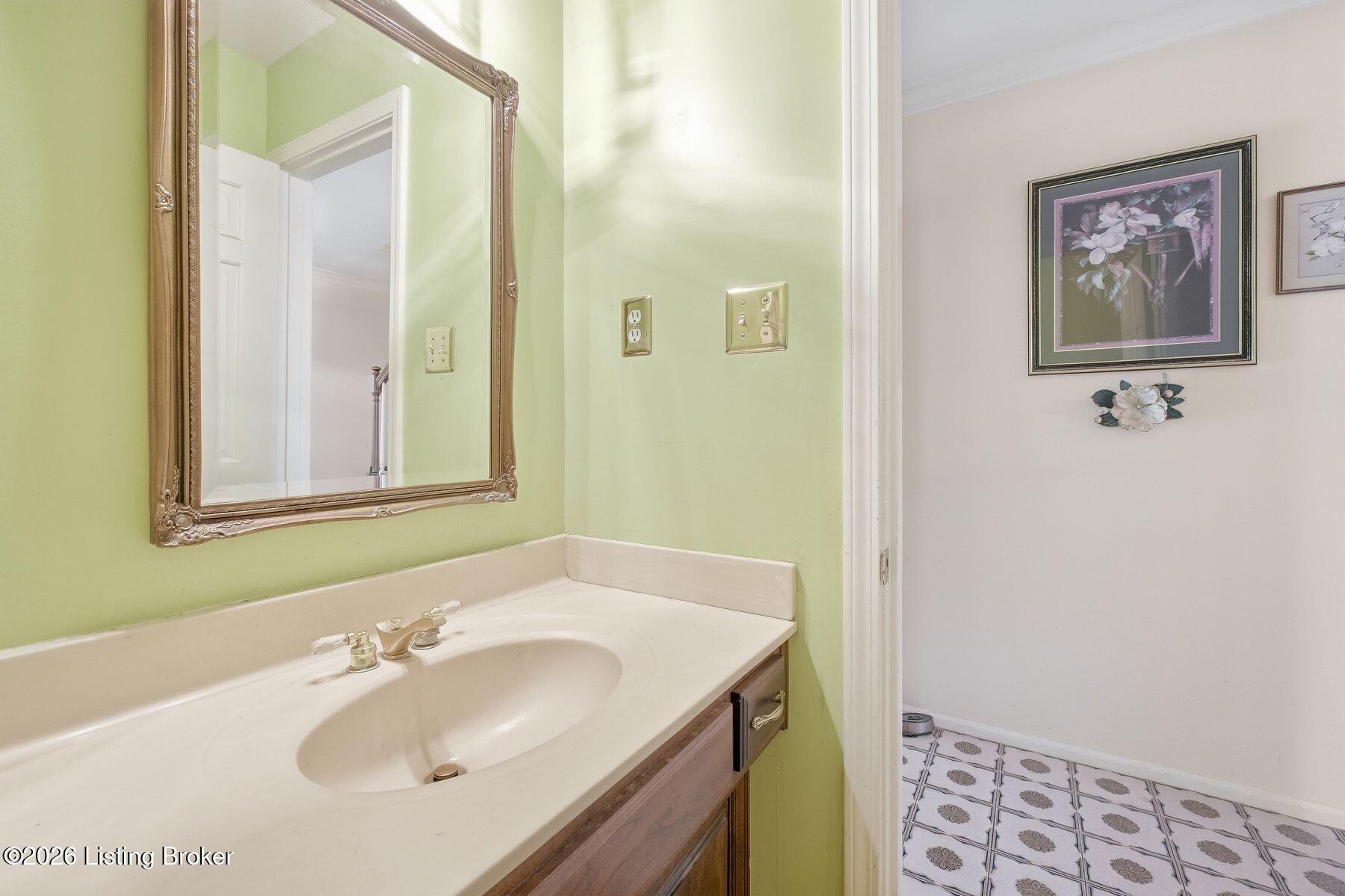 Bathroom vanity with an oval sink and ornate mirror beside a room with patterned tile flooring.