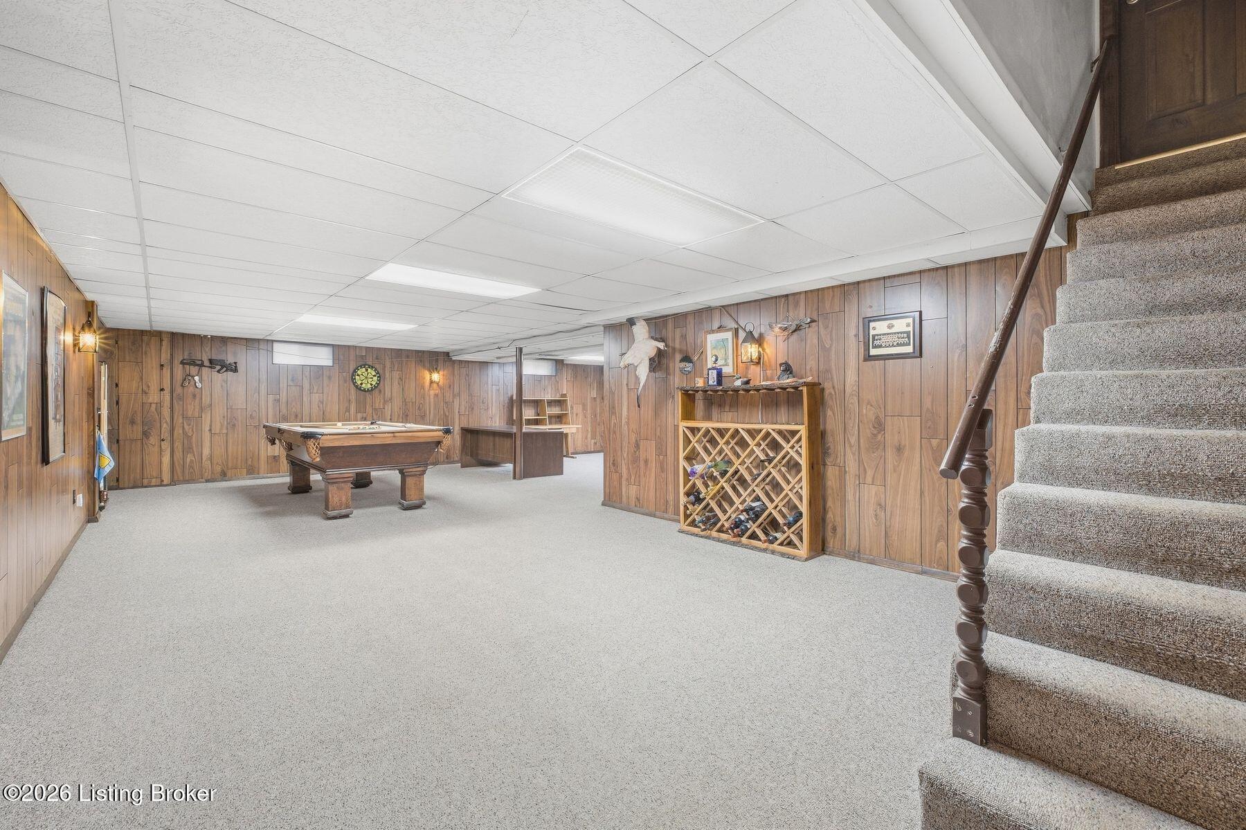Basement recreation room with a pool table, wood-paneled walls, and carpeted stairs.