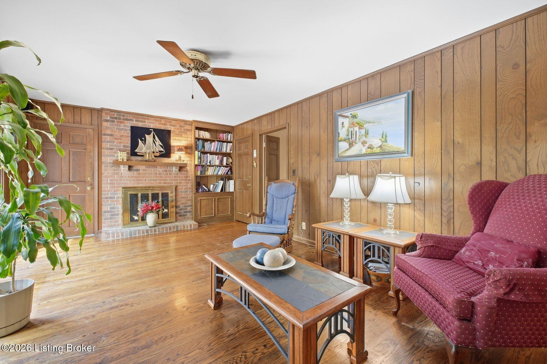 Living room with a brick fireplace, built-in bookshelves, wood-paneled walls, and burgundy seating.
