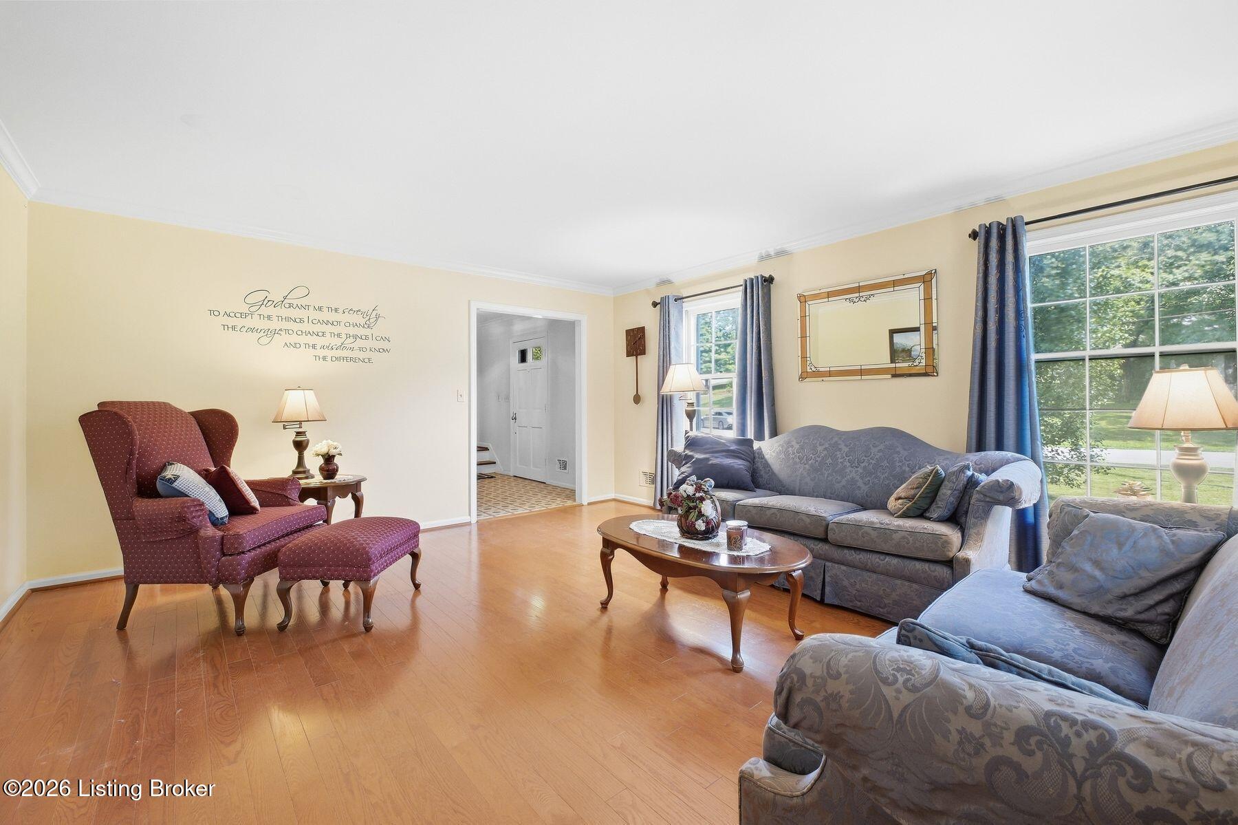 Living room with blue sofas, a burgundy wingback chair, hardwood floors, and large windows.