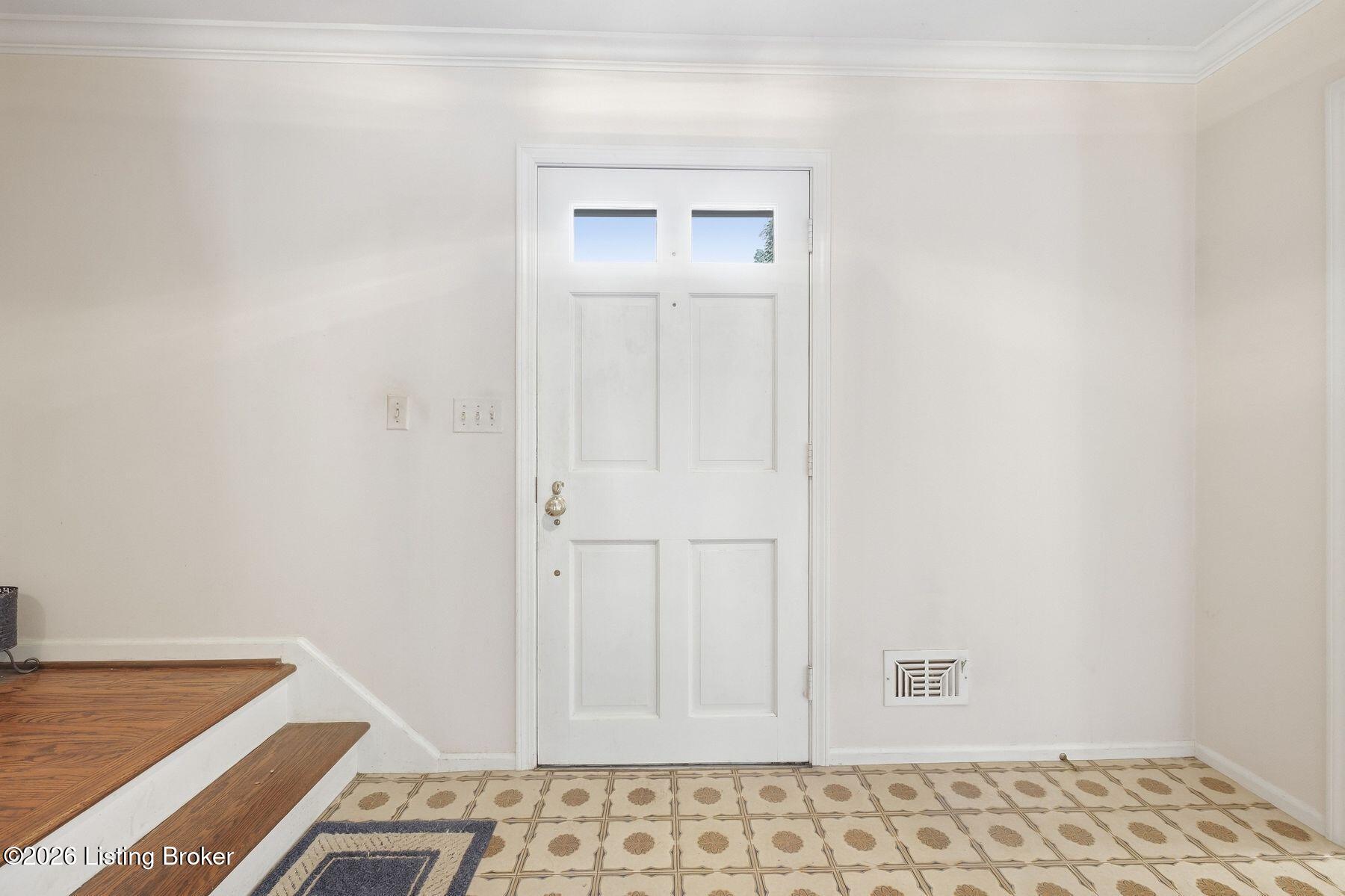 Entryway with a white paneled front door, patterned tile floor, and staircase with wood treads.