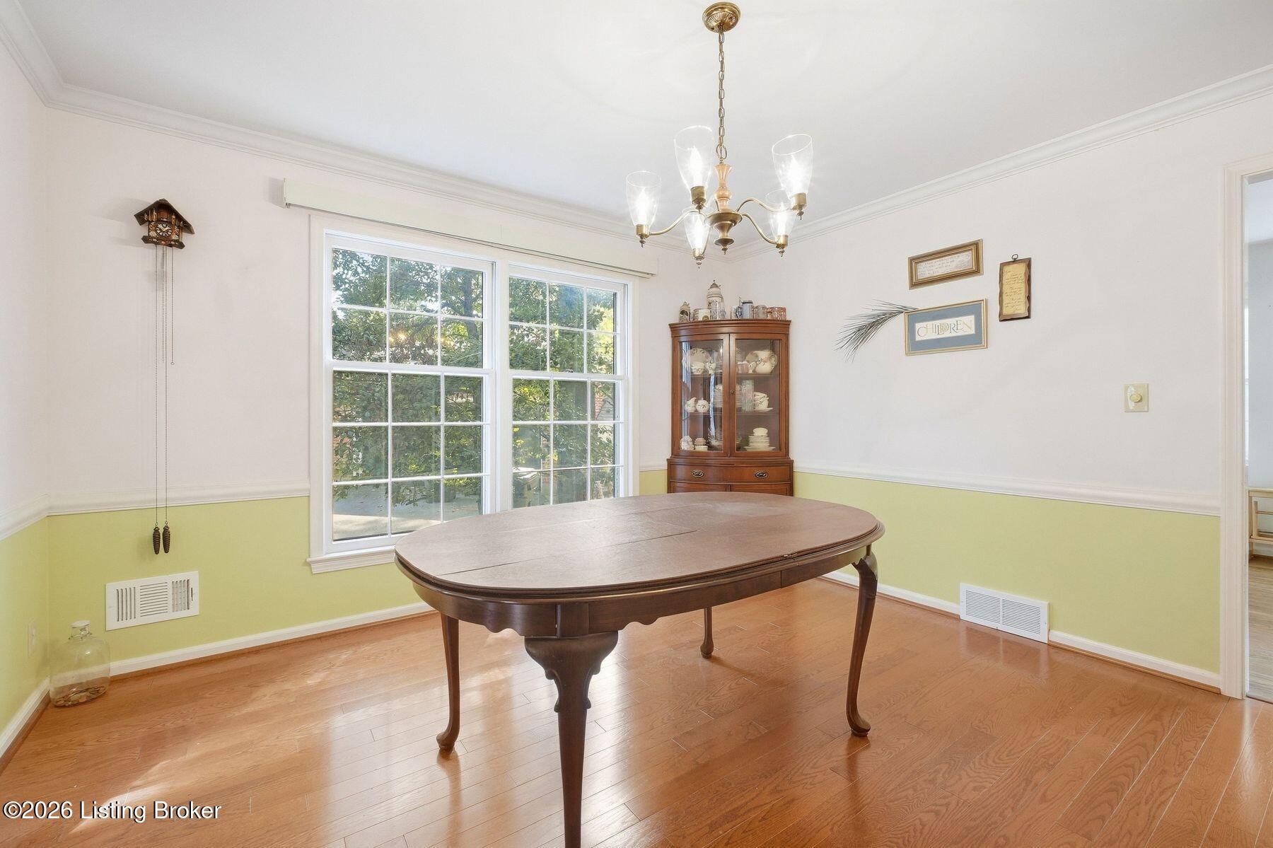 Dining room with an oval wooden table, glass-front china cabinet, and leafy views through large windows.